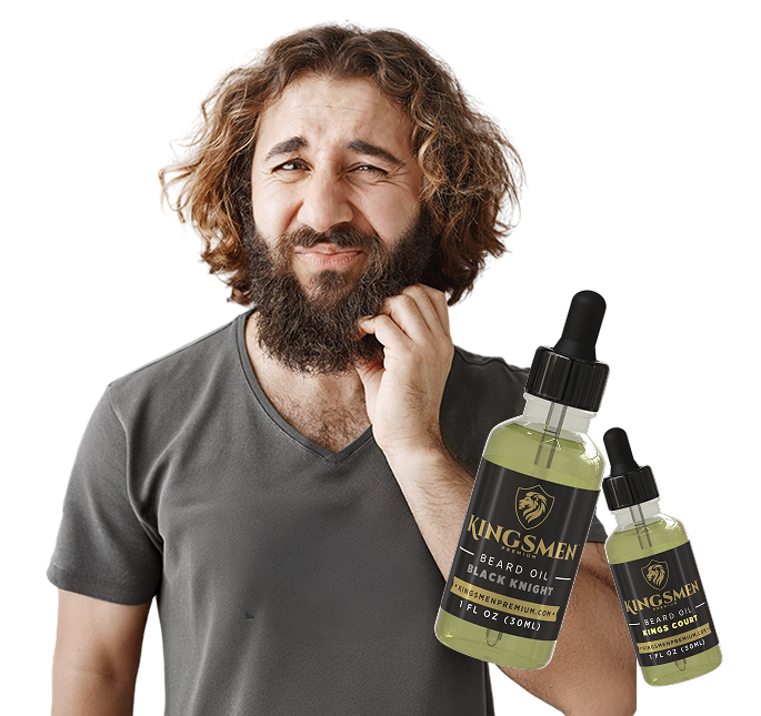 A man with a full beard and wavy hair holds two dropper bottles of Kingsmen Beard Oil against a plain white background. The bottles are filled with a pale yellow-green oil and have black labels with gold lettering.