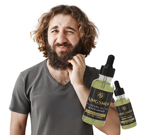 A man with a full beard and wavy hair holds two dropper bottles of Kingsmen Beard Oil against a plain white background. The bottles are filled with a pale yellow-green oil and have black labels with gold lettering.-mobile