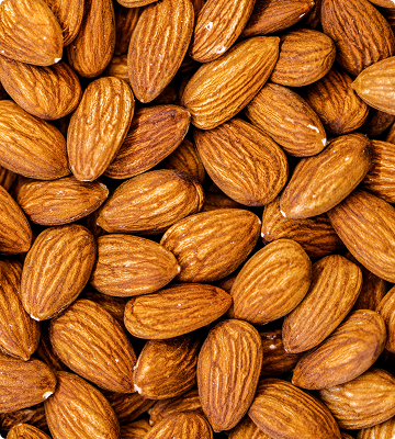 A close-up pile of whole almonds filling the frame, showing their natural brown and tan striped skins.
